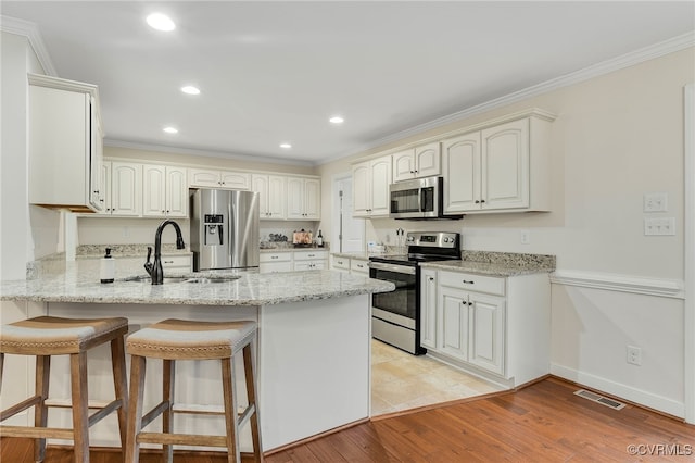 kitchen with crown molding, visible vents, appliances with stainless steel finishes, a sink, and a peninsula