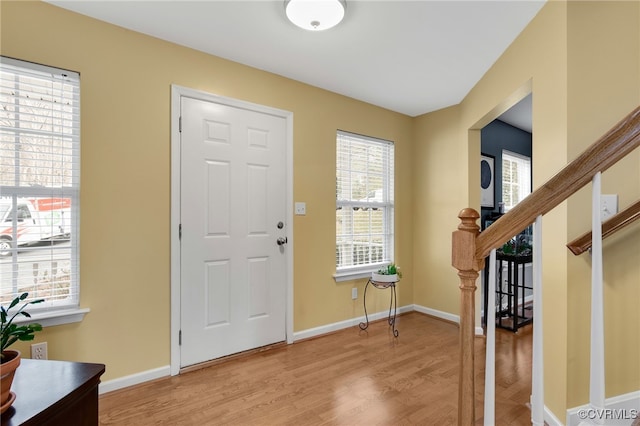 foyer entrance with light wood-style floors, baseboards, and stairway