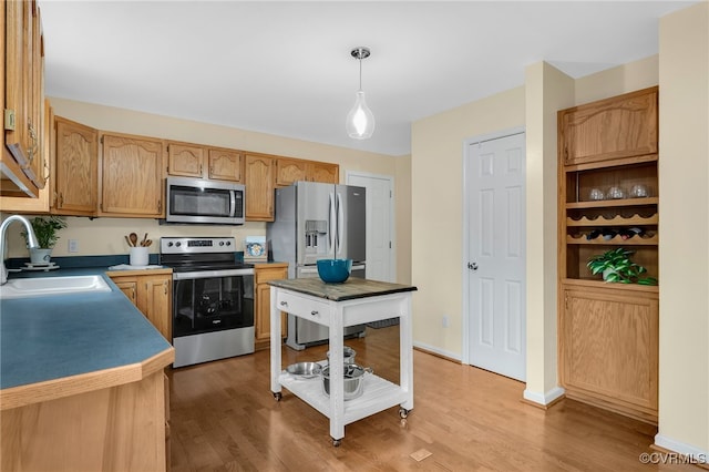 kitchen with appliances with stainless steel finishes, light wood-type flooring, a sink, and hanging light fixtures