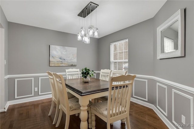 dining space featuring a wainscoted wall, dark wood finished floors, a decorative wall, and an inviting chandelier