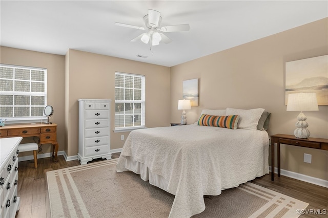 bedroom with a ceiling fan, visible vents, baseboards, and wood finished floors