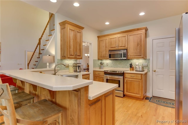 kitchen with a breakfast bar area, stainless steel appliances, a peninsula, a sink, and light wood finished floors