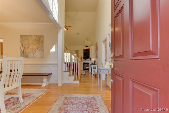 entrance foyer featuring a decorative wall, a ceiling fan, stairs, ornamental molding, and light wood-type flooring