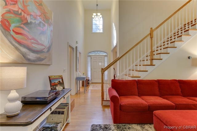 living area with stairs, a high ceiling, an inviting chandelier, and wood finished floors