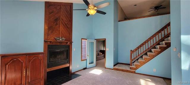 interior space with ceiling fan, a fireplace, a towering ceiling, baseboards, and stairs