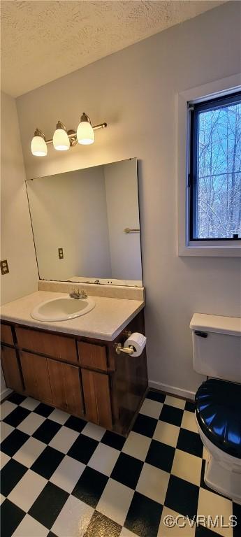 half bath featuring toilet, a textured ceiling, vanity, and tile patterned floors