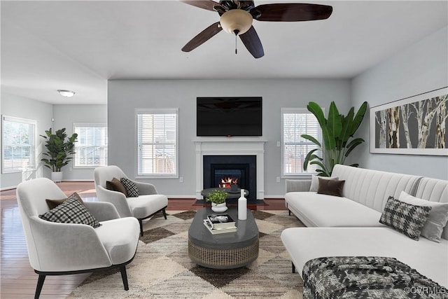 living room with ceiling fan, a glass covered fireplace, and wood finished floors