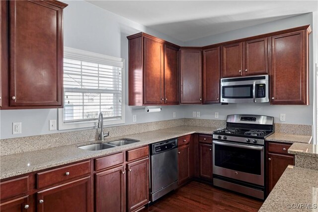 kitchen with dark wood-style floors, appliances with stainless steel finishes, a sink, and light stone countertops