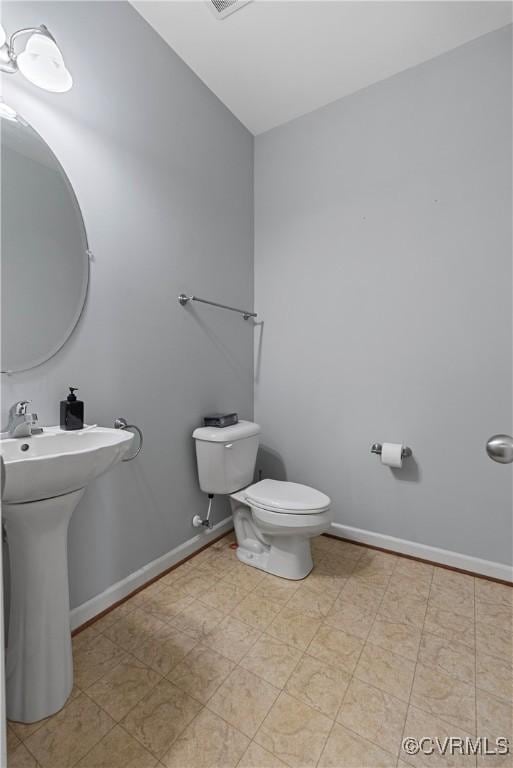 half bath featuring toilet, baseboards, and a sink