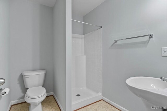 bathroom with toilet, a shower stall, baseboards, and a sink