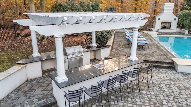 view of patio / terrace featuring exterior fireplace, outdoor wet bar, area for grilling, fence, and a grill