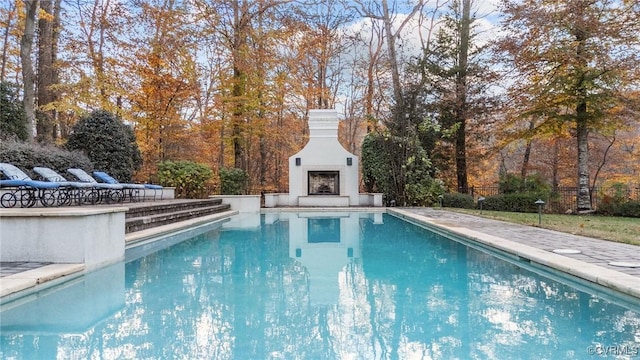 pool with a patio, an outdoor fireplace, and fence