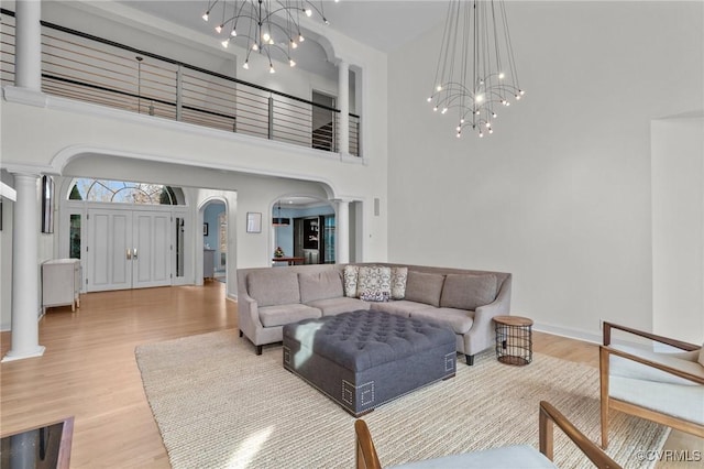 living area featuring a chandelier, arched walkways, ornate columns, and wood finished floors