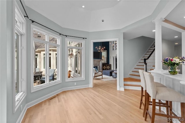 interior space featuring visible vents, light wood-style floors, stairway, a glass covered fireplace, and decorative columns