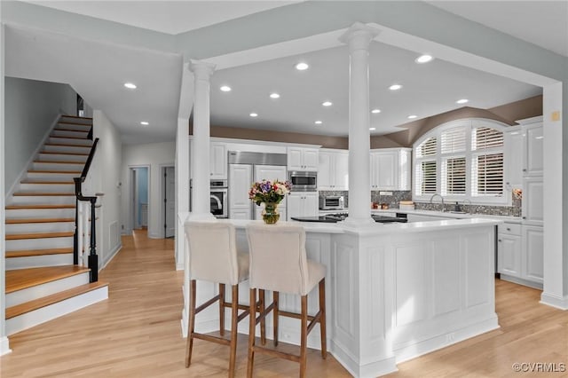 kitchen featuring tasteful backsplash, white cabinetry, built in appliances, light wood-type flooring, and ornate columns