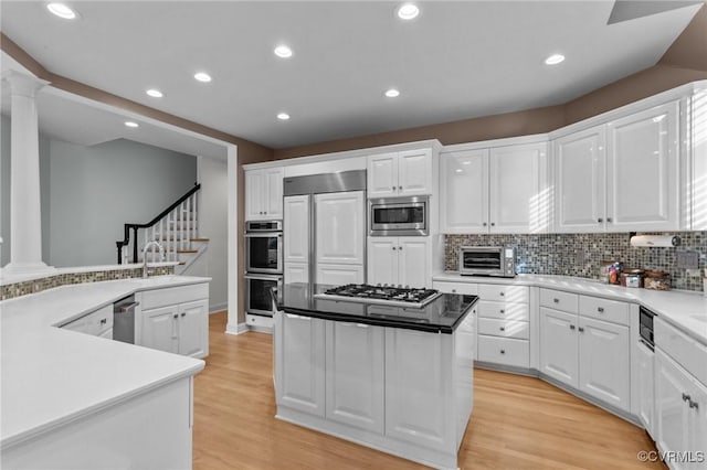 kitchen featuring a kitchen island, built in appliances, light wood-type flooring, ornate columns, and white cabinetry