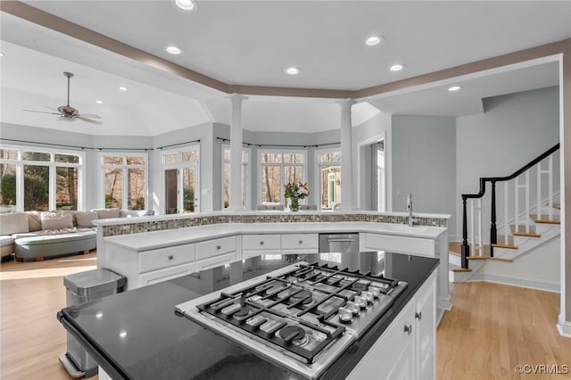 kitchen featuring light wood finished floors, appliances with stainless steel finishes, open floor plan, ornate columns, and a sink