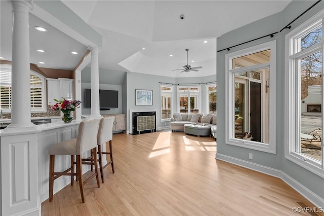 interior space with a kitchen breakfast bar, white cabinets, light countertops, light wood finished floors, and ornate columns