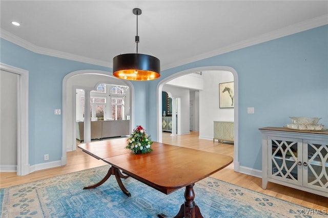 dining room with arched walkways, light wood-style floors, baseboards, and crown molding