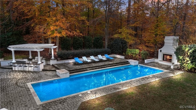 outdoor pool with a patio area, a lit fireplace, and a pergola