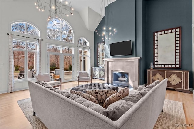 living room featuring a chandelier, a high ceiling, a fireplace, wood finished floors, and french doors