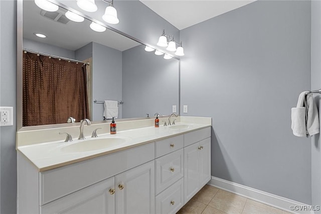 bathroom featuring baseboards, double vanity, a sink, and tile patterned floors