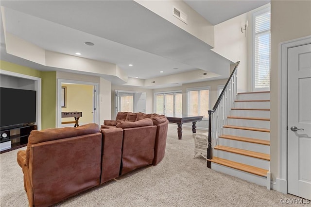 carpeted living area with visible vents, a tray ceiling, stairway, and a wealth of natural light