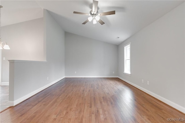 empty room featuring vaulted ceiling, ceiling fan with notable chandelier, wood finished floors, and baseboards