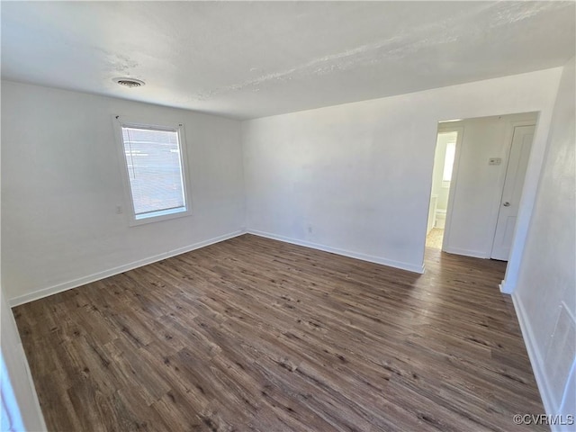 empty room featuring dark wood-style floors, visible vents, and baseboards