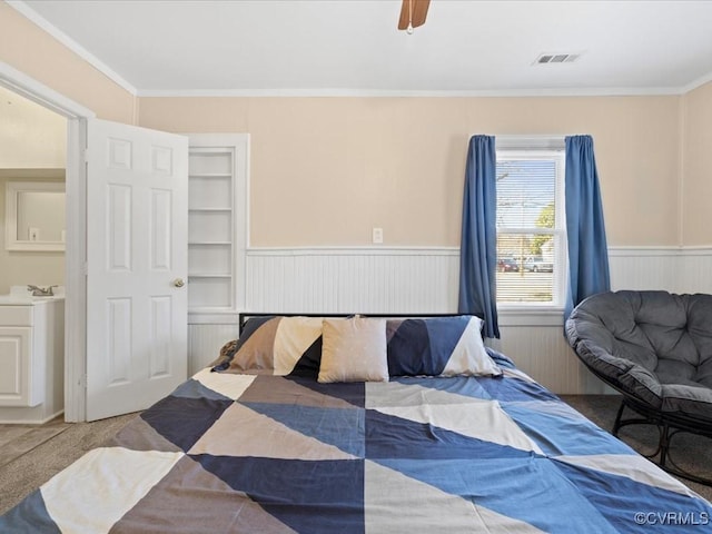 carpeted bedroom with visible vents, a wainscoted wall, ceiling fan, ornamental molding, and a sink