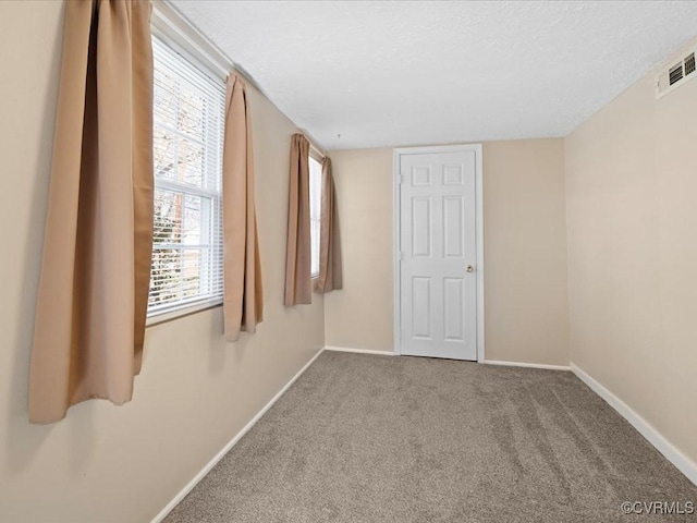 carpeted empty room featuring baseboards, visible vents, and a textured ceiling