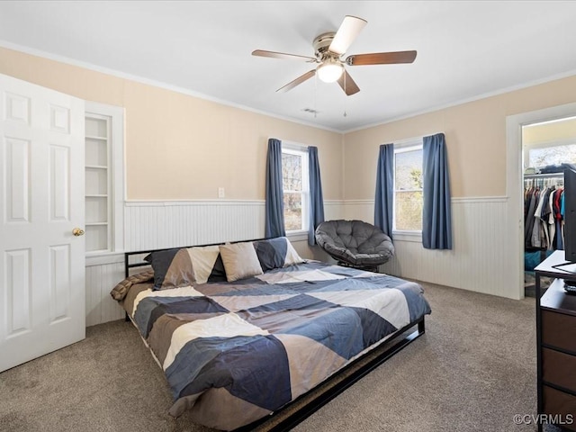 bedroom with a wainscoted wall, carpet floors, ceiling fan, and crown molding