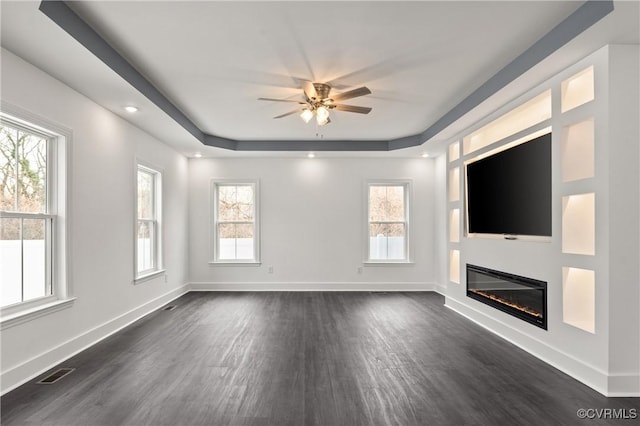 unfurnished living room with a tray ceiling, visible vents, and baseboards