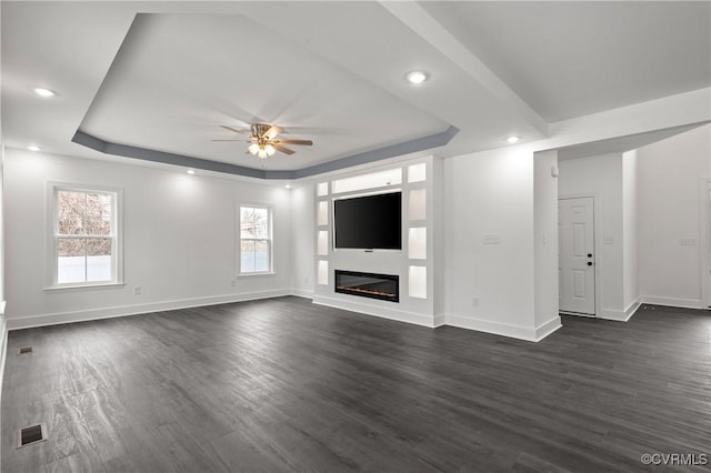 unfurnished living room with visible vents, a tray ceiling, dark wood-type flooring, and a glass covered fireplace