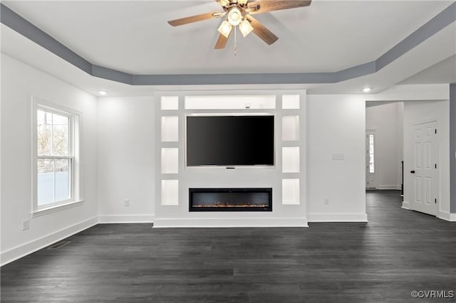 unfurnished living room featuring ceiling fan, baseboards, dark wood finished floors, and a glass covered fireplace