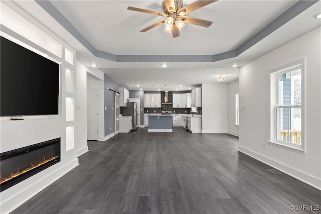 unfurnished living room featuring baseboards, a raised ceiling, dark wood-type flooring, and a glass covered fireplace