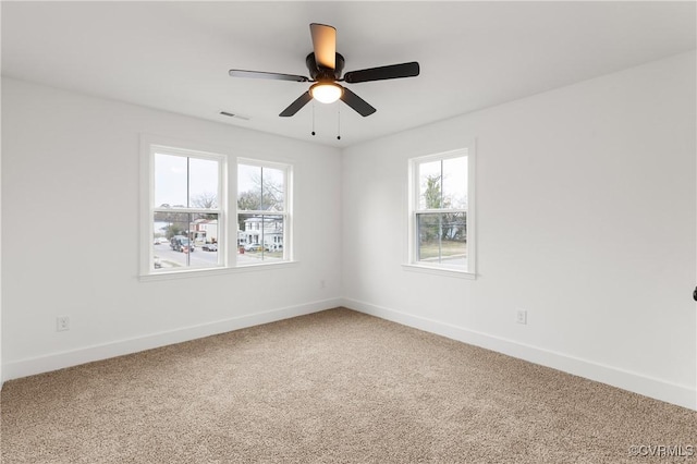 empty room featuring light carpet, a ceiling fan, visible vents, and baseboards