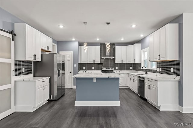 kitchen with a barn door, stainless steel appliances, white cabinetry, wall chimney range hood, and a center island