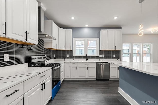 kitchen with appliances with stainless steel finishes, white cabinets, a sink, and wall chimney range hood