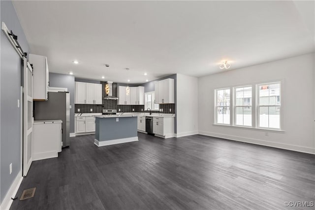 kitchen featuring a barn door, stainless steel appliances, a wealth of natural light, a center island, and wall chimney exhaust hood