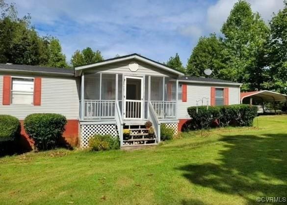 back of property with a sunroom, a lawn, and a detached carport