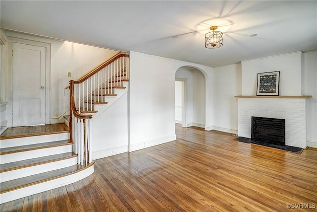 unfurnished living room featuring baseboards, stairway, a fireplace, wood finished floors, and arched walkways