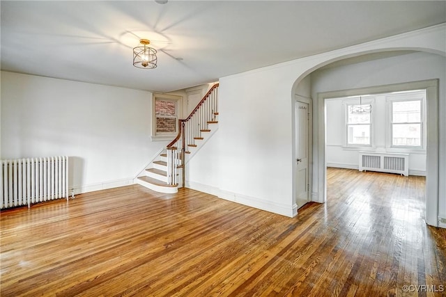 spare room featuring radiator, stairs, radiator heating unit, hardwood / wood-style flooring, and arched walkways