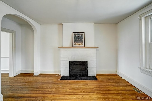 unfurnished living room with visible vents, baseboards, ornamental molding, wood finished floors, and arched walkways