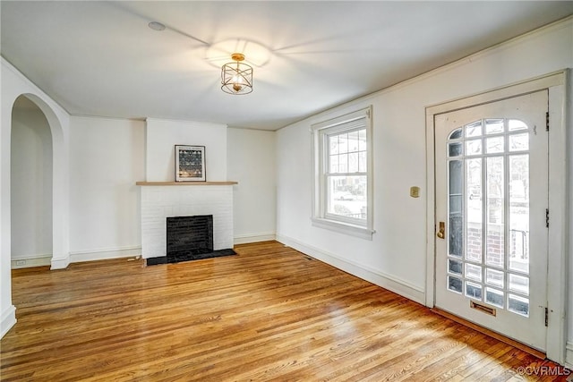 unfurnished living room with a brick fireplace, wood finished floors, arched walkways, and baseboards