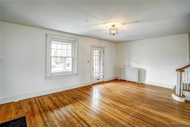 unfurnished living room with visible vents, baseboards, radiator, and wood finished floors