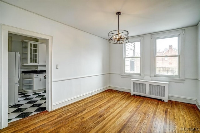 unfurnished dining area with tile patterned floors, baseboards, radiator heating unit, and an inviting chandelier