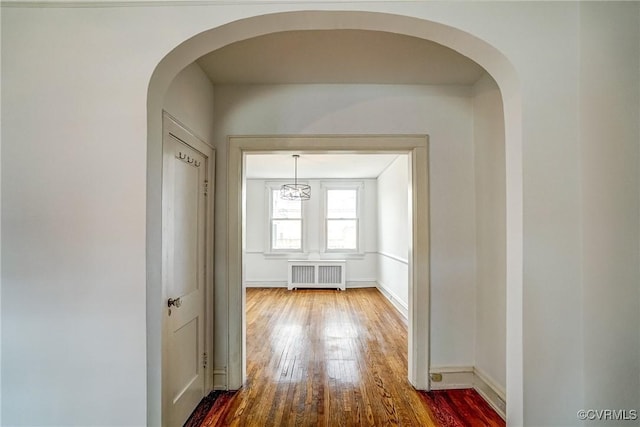 hall with radiator heating unit, arched walkways, dark wood-style flooring, and baseboards