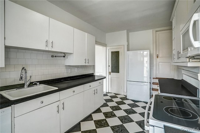 kitchen with dark countertops, tasteful backsplash, dark floors, white appliances, and a sink