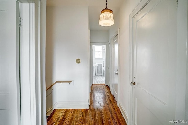 corridor featuring an upstairs landing, dark wood-type flooring, and baseboards